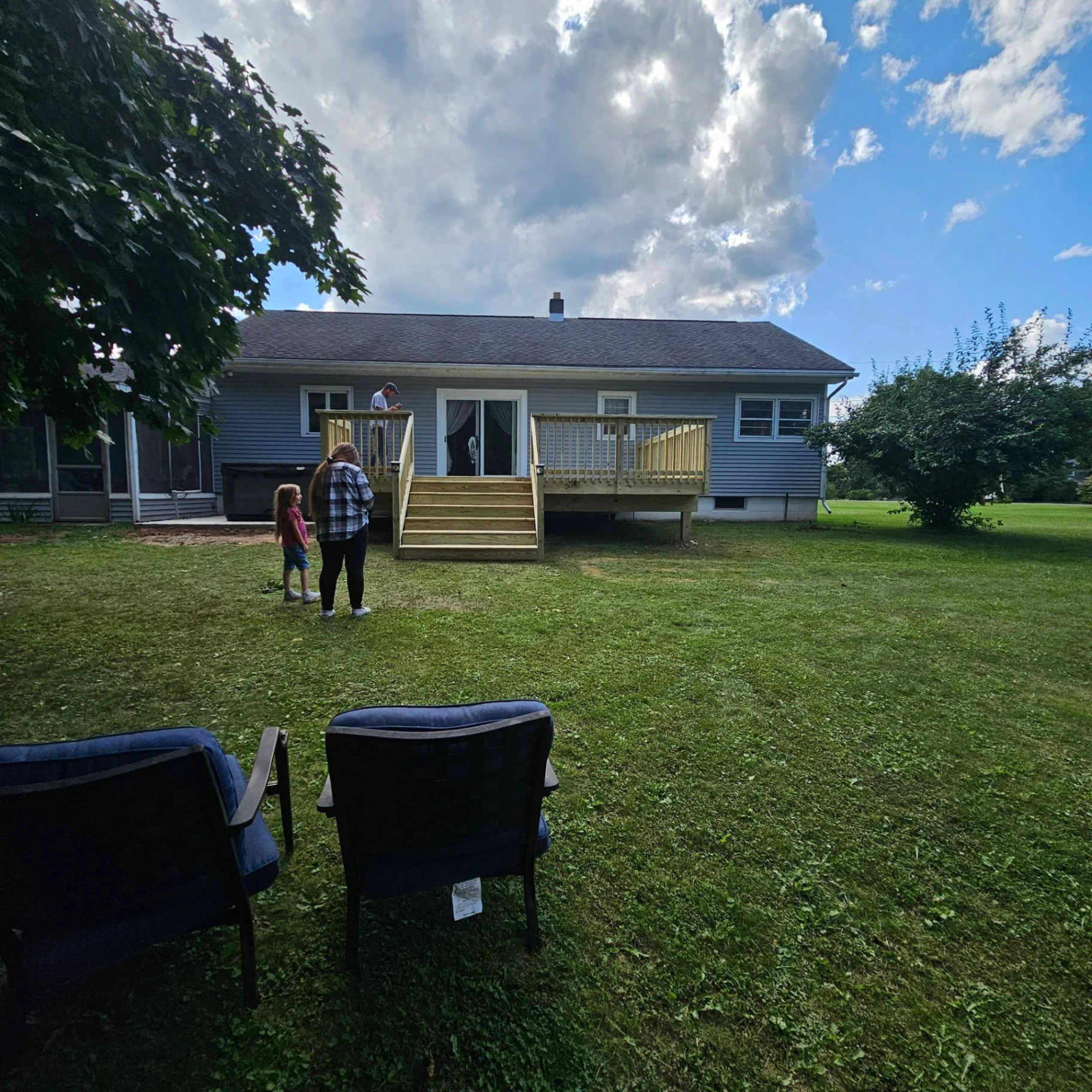Finished back deck with stairs on a blue ranch home with the homeowner family standing in the yard