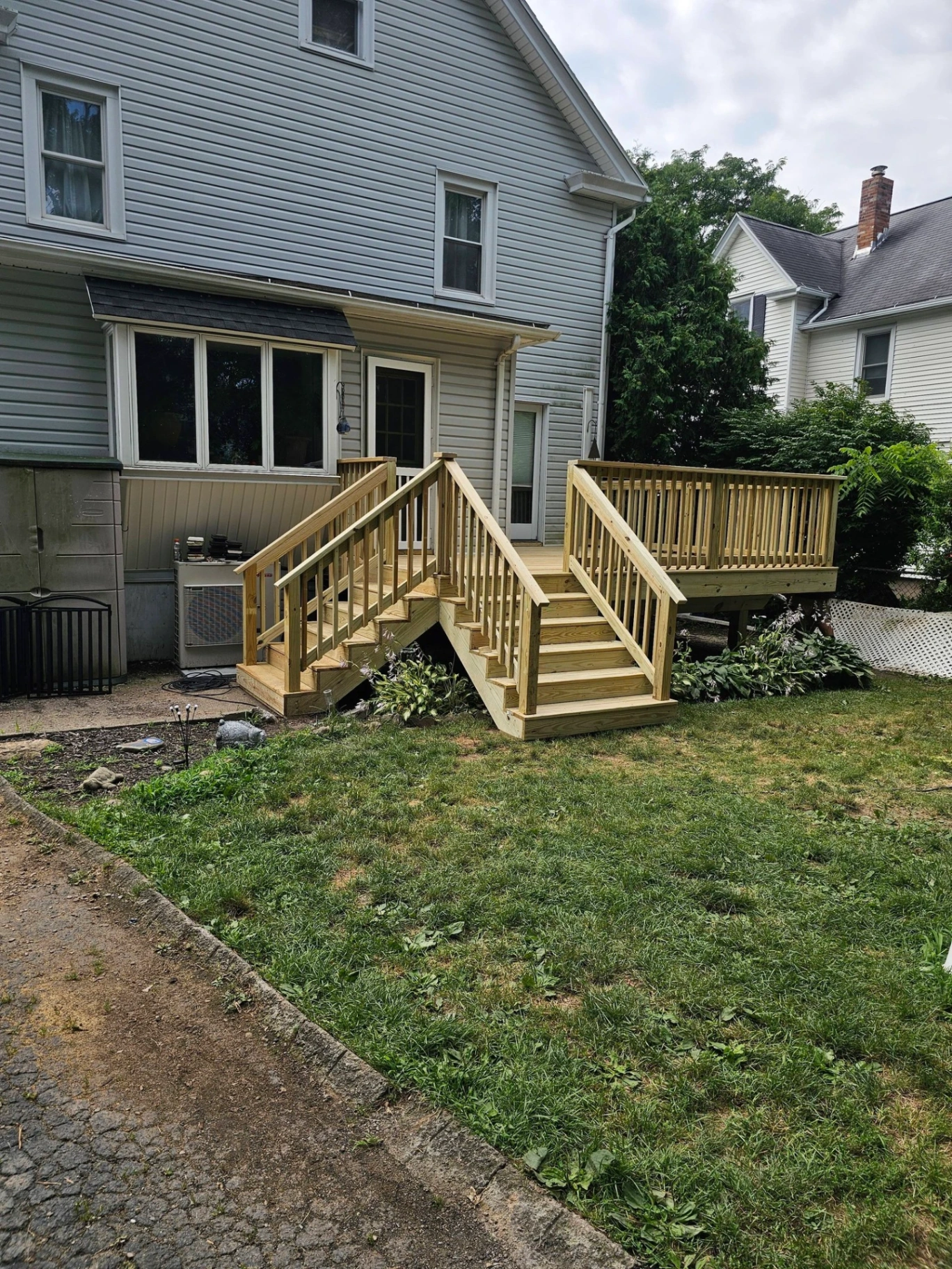 Back deck with split pressure treated stairs and railings on a blue two story home
