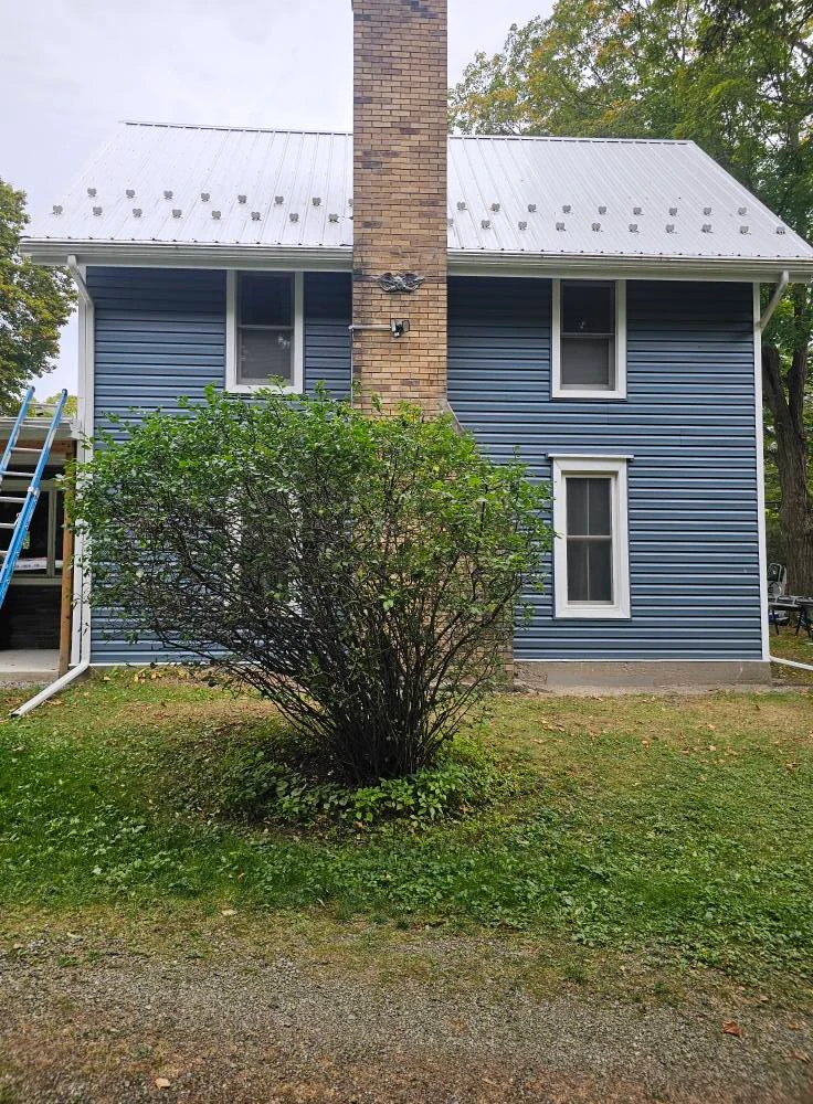 Rear elevation of a blue sided farmhouse with brick chimney and new metal roof