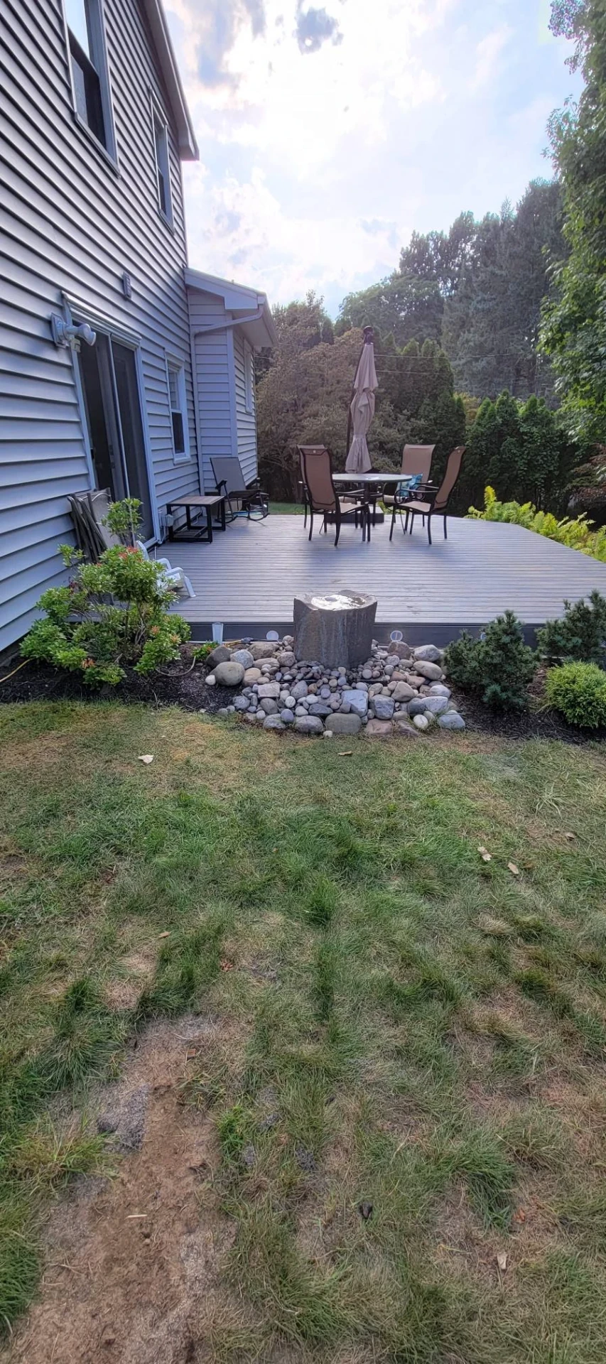 Low profile composite deck on a gray home with landscaped river rock fountain bed in front
