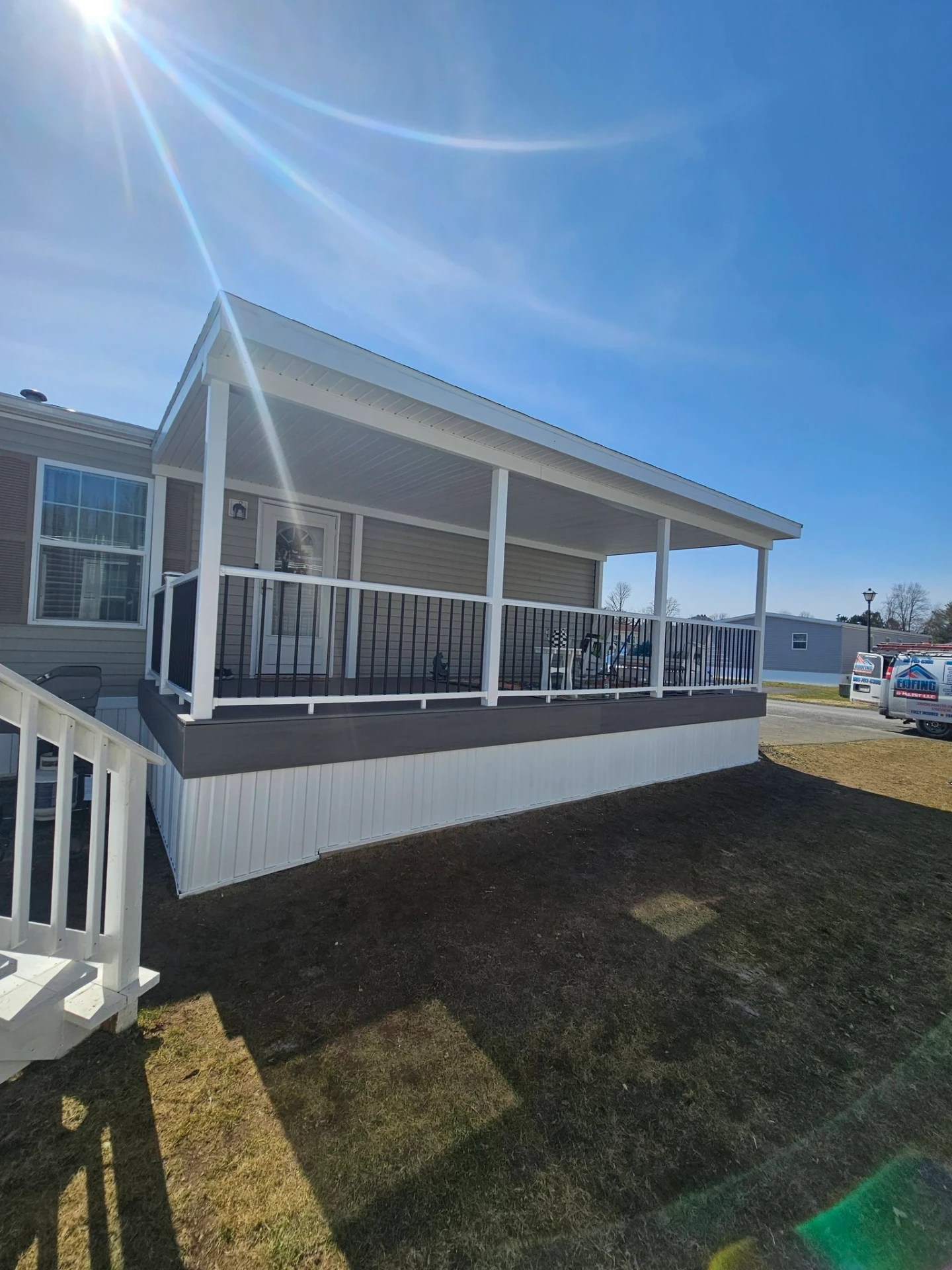 Covered manufactured home porch with white posts, black aluminum railings and enclosed skirting