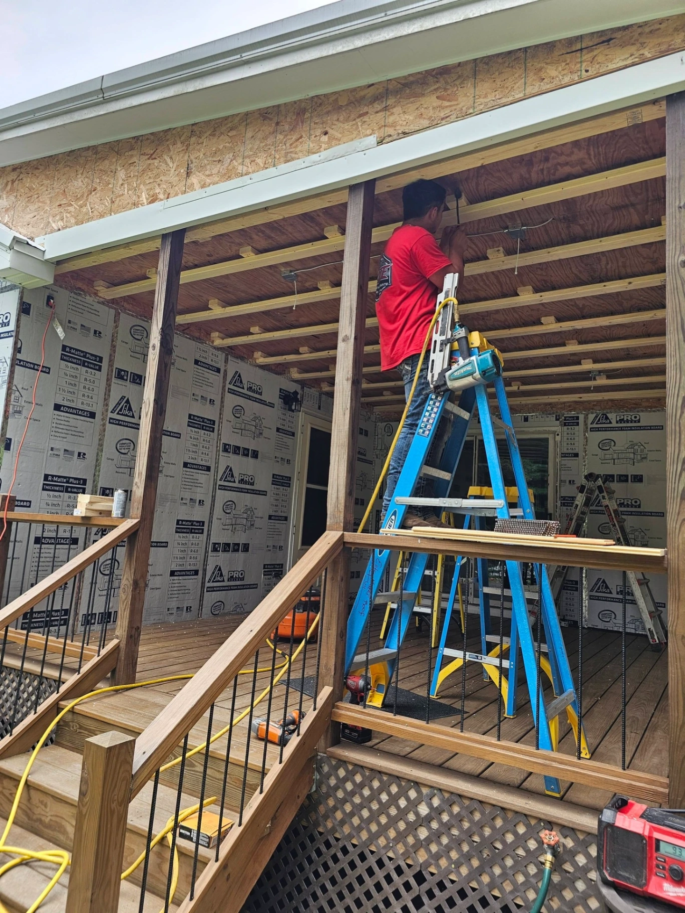 Crew member installing tongue and groove ceiling under a covered porch addition with foam insulation board behind