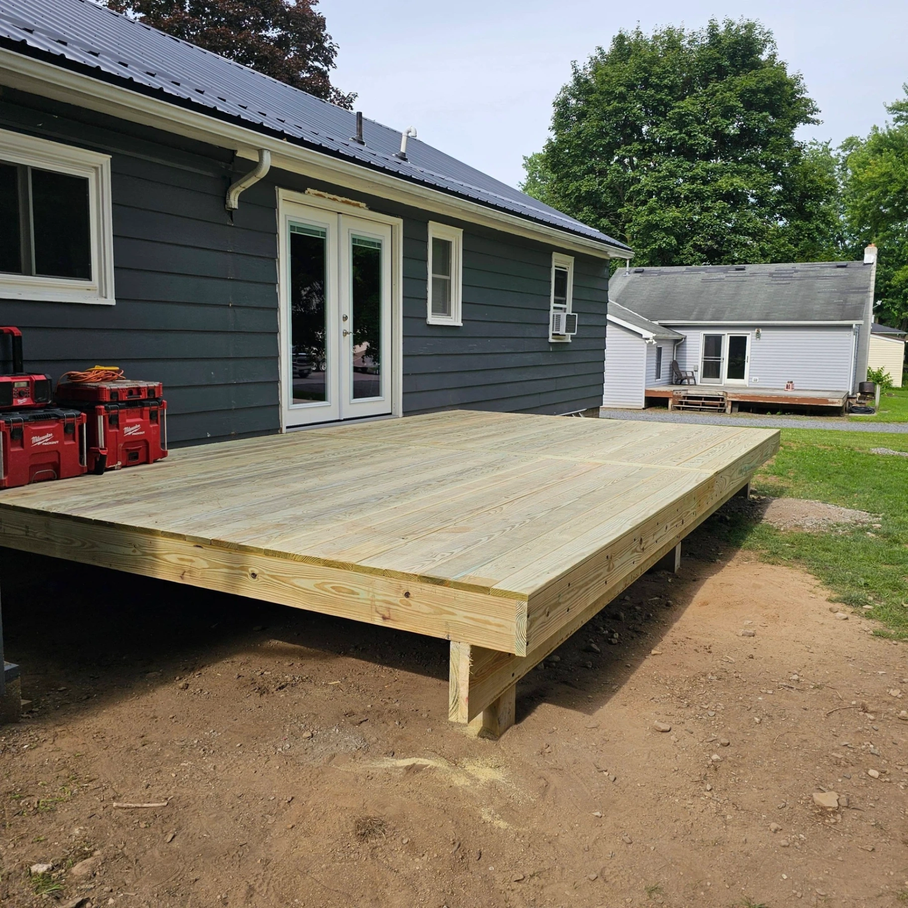 Low profile floating deck off French doors on a dark gray sided home with new metal roof