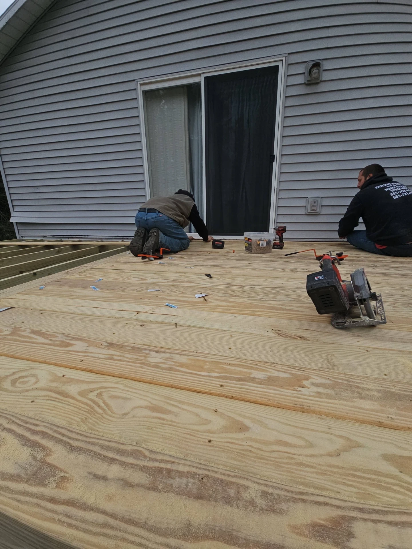 Eastside Roofing crew installing pressure treated deck boards on a gray sided home
