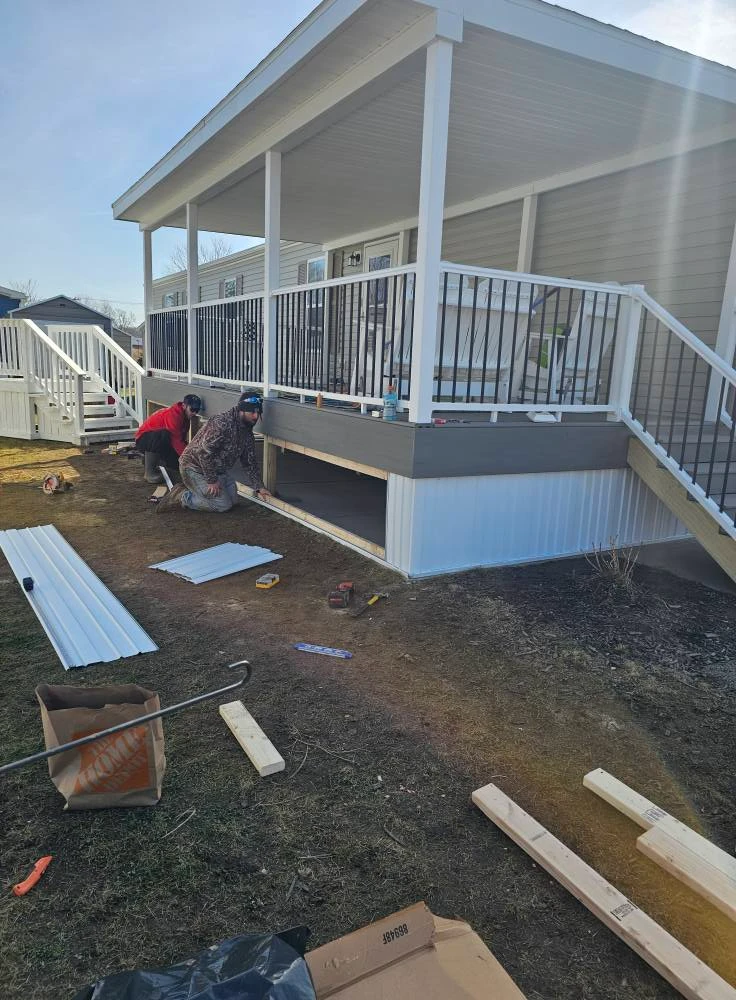 Crew installing white skirting under a finished covered deck with aluminum railings