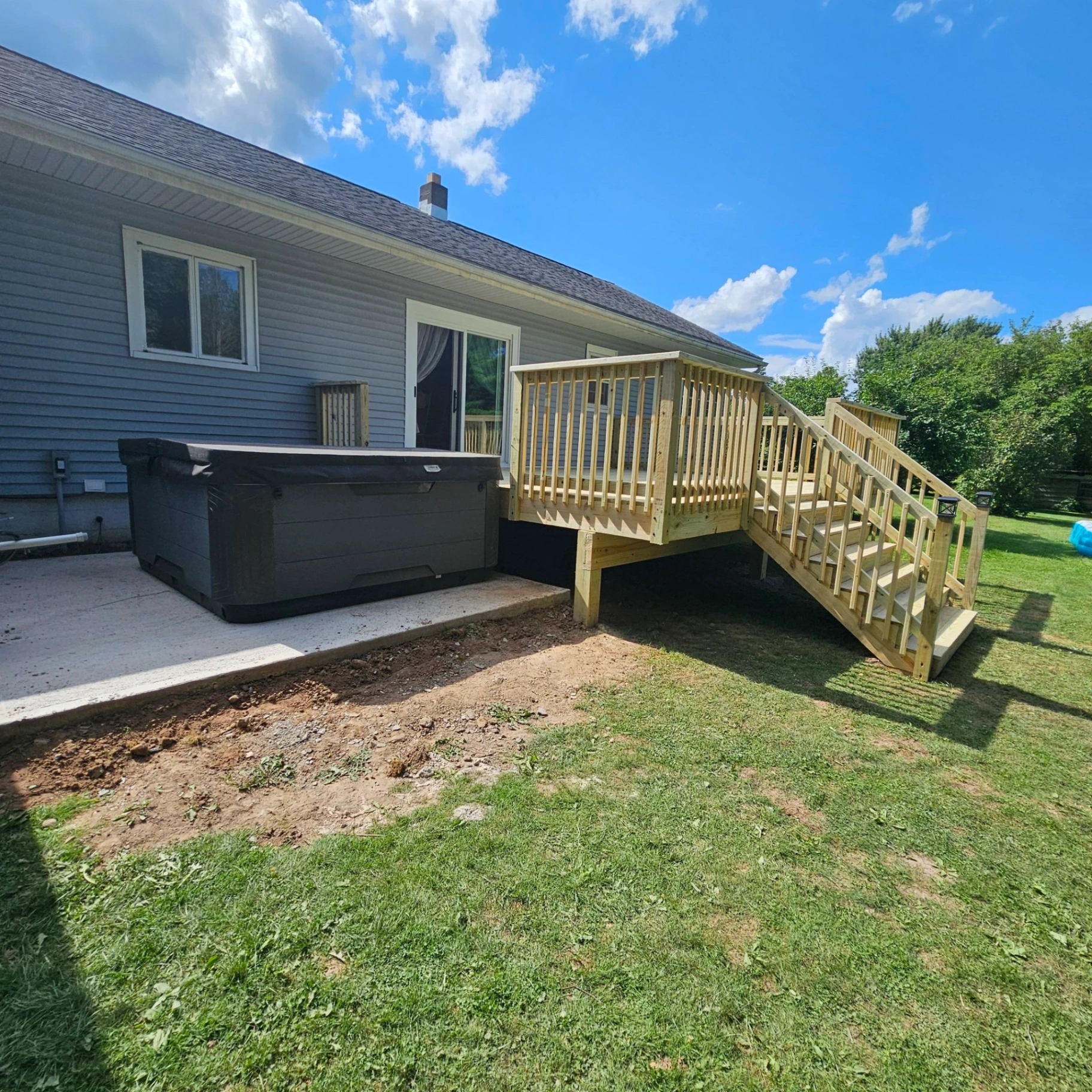 Pressure treated backyard deck with railings and stairs built next to a concrete hot tub pad