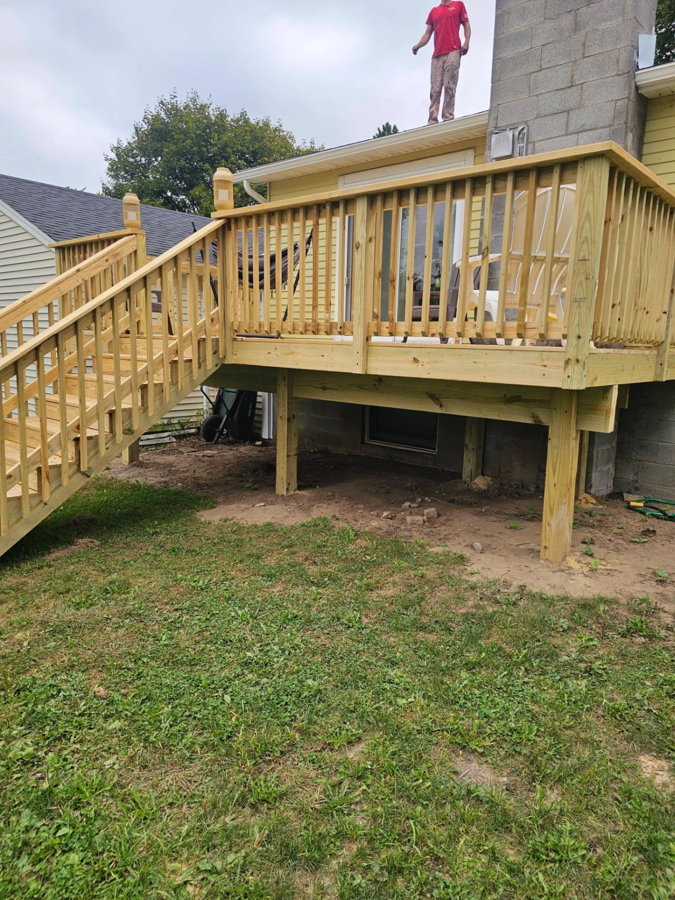 Side view of an elevated deck build with stairs and a worker visible on the roof above