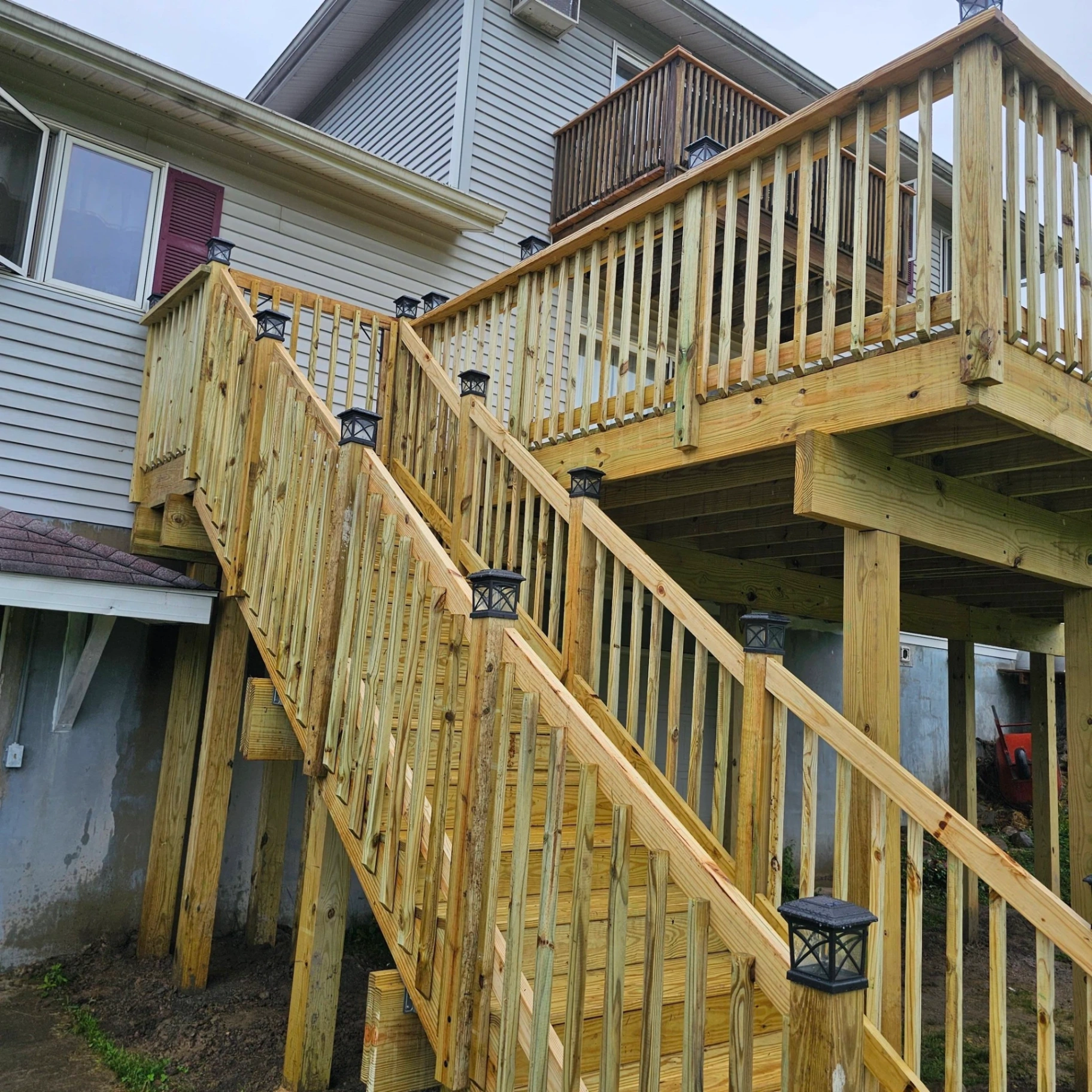 Tall elevated deck with full pressure treated staircase, wood railings and black solar post cap lights