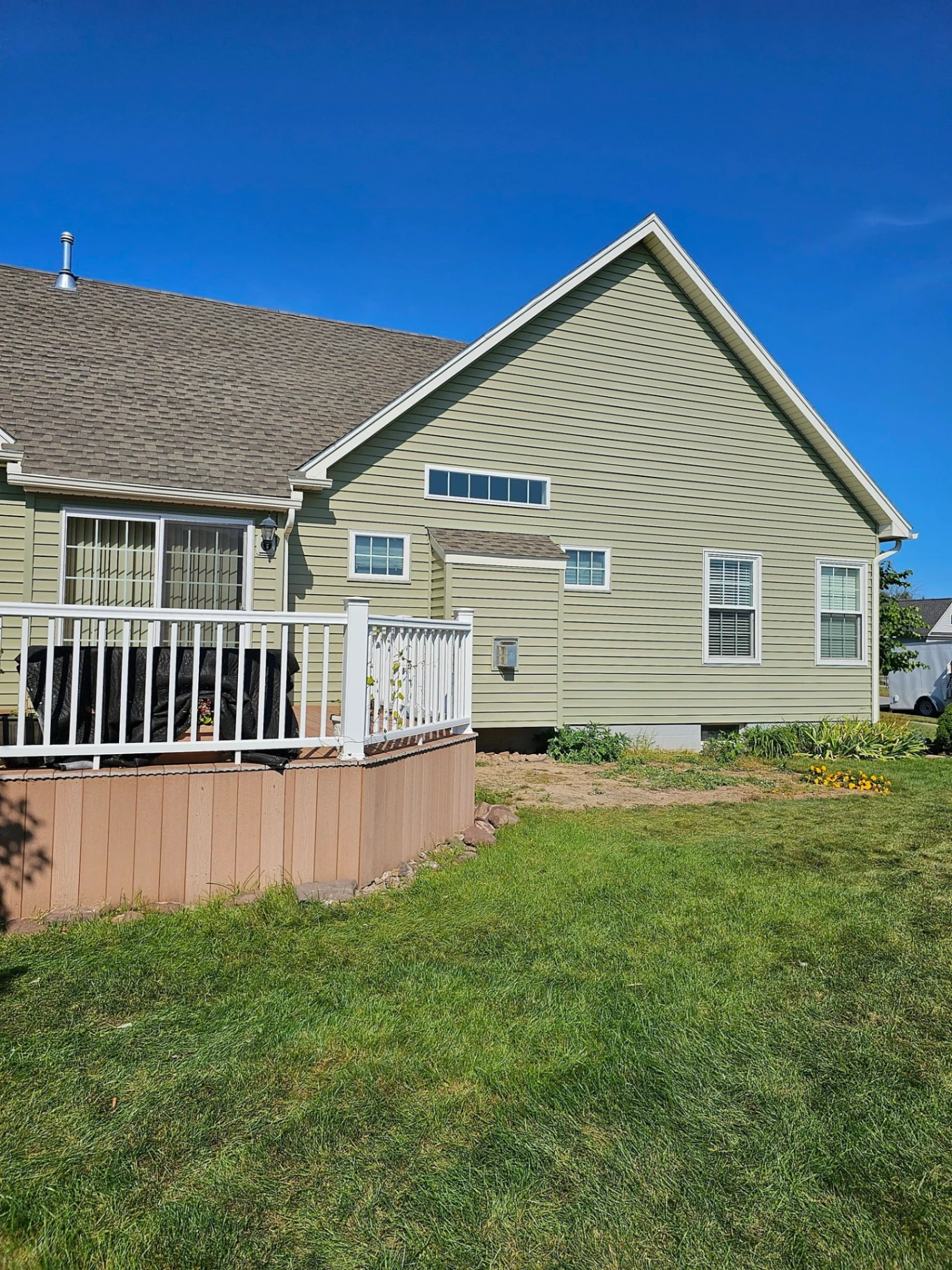 Sage green sided home with white vinyl railing deck and brown skirting on the side elevation
