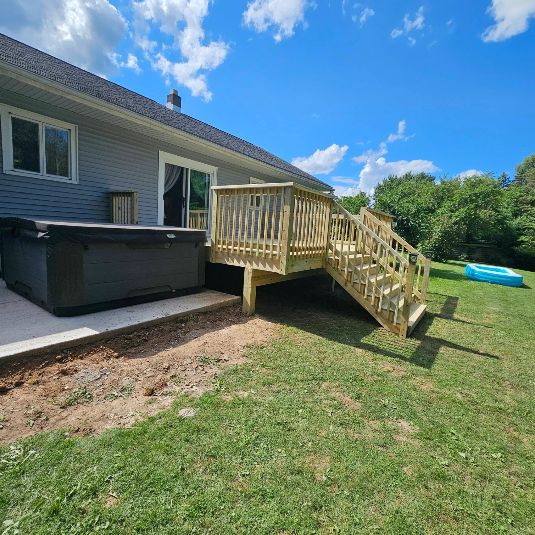 Pressure treated side deck with stairs and railings next to a hot tub on a gray ranch home