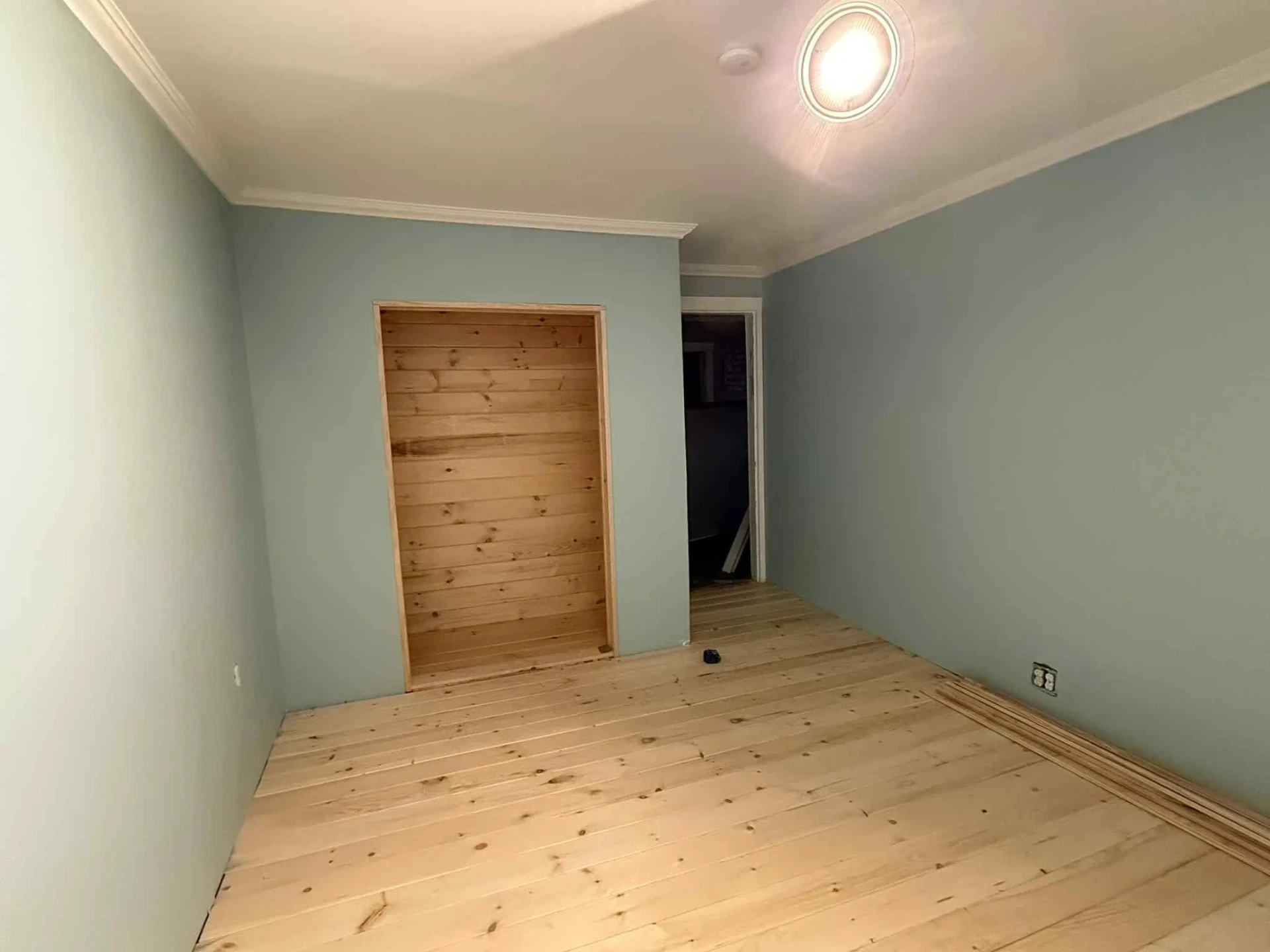 Remodeled bedroom with soft blue walls, white crown molding, pine plank floors and a built in pine closet alcove