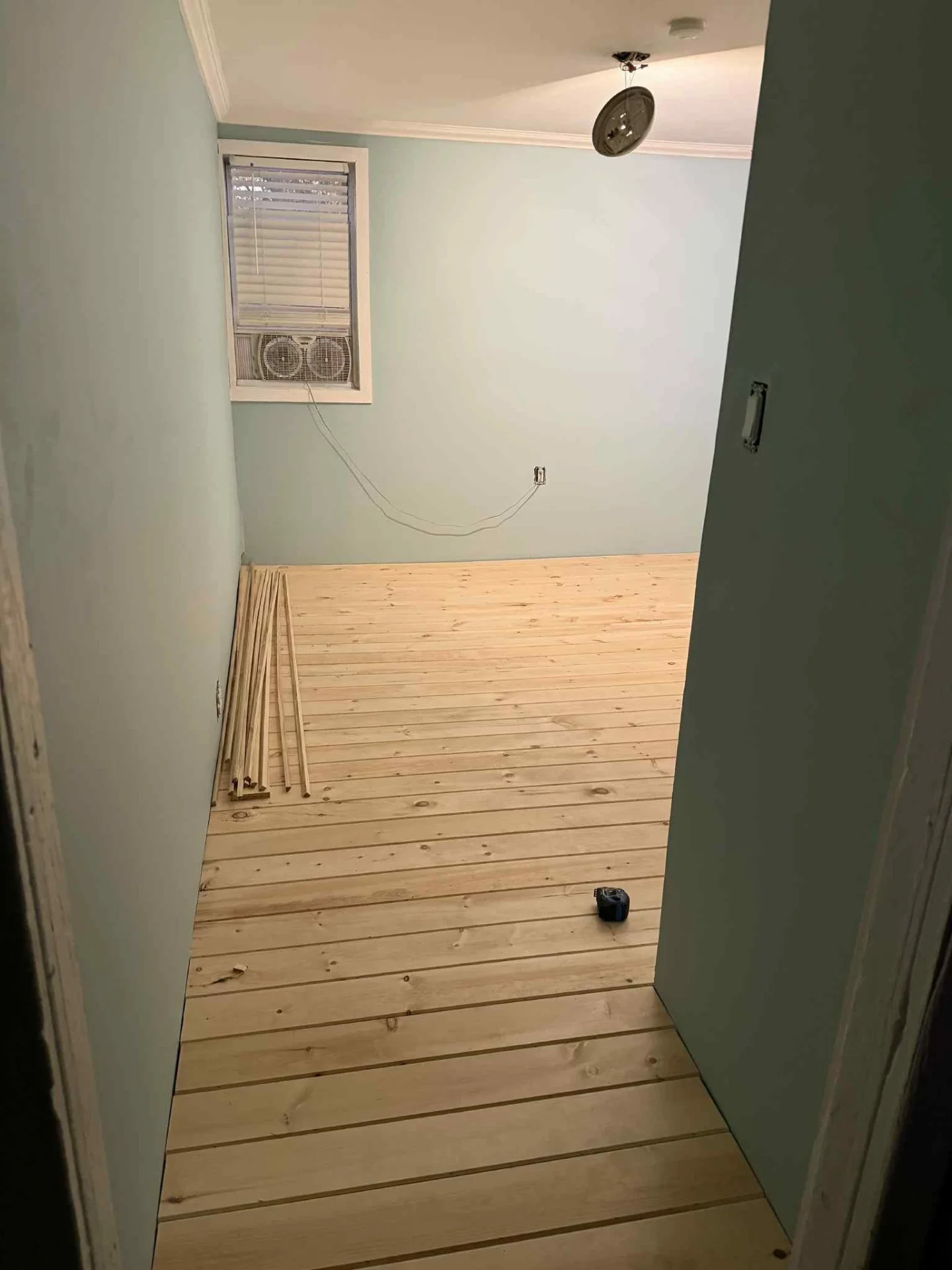 Wide pine plank flooring partway through install in a freshly painted blue room
