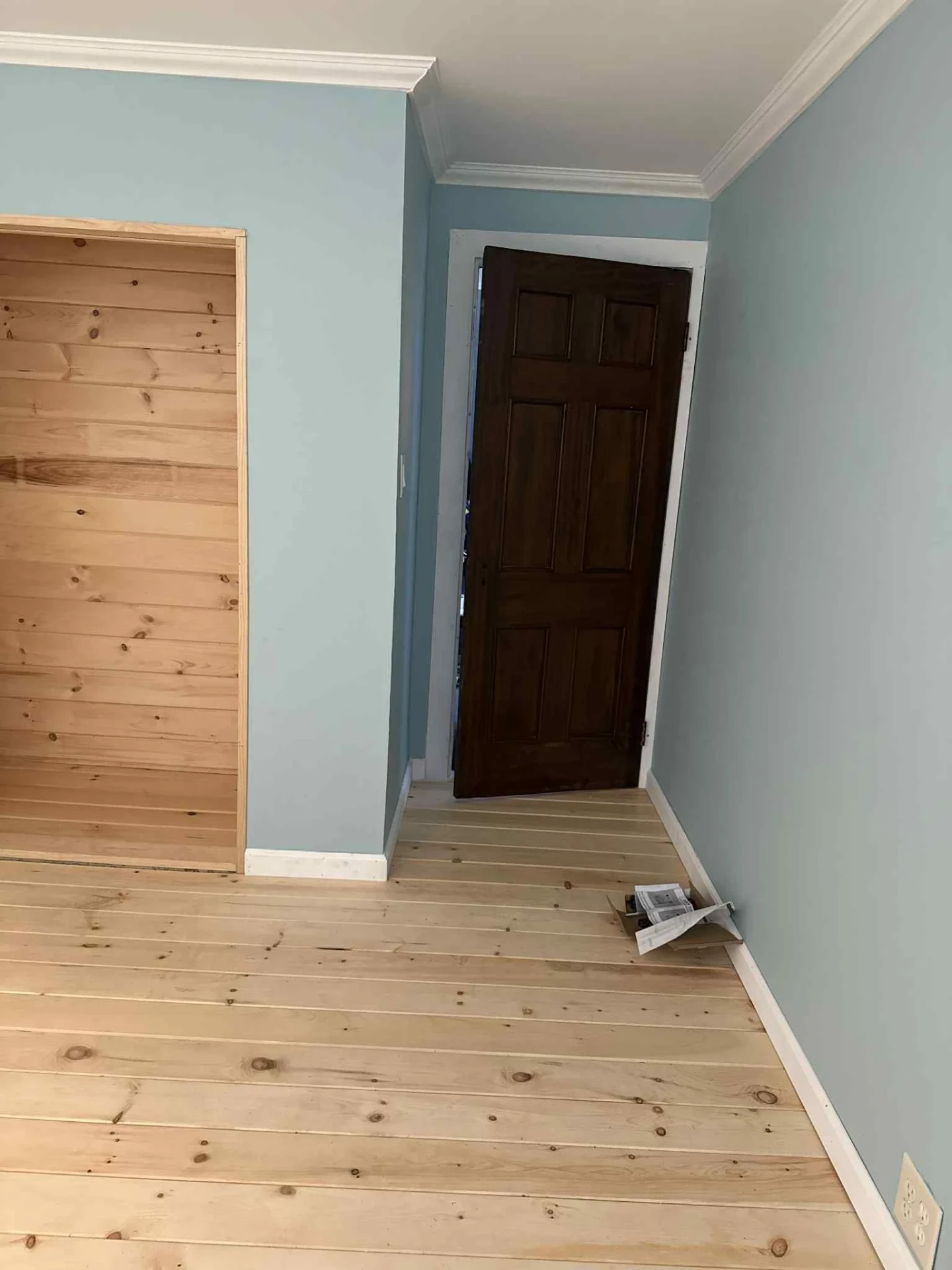Stained six panel solid wood interior door installed next to a built in pine closet alcove with blue walls