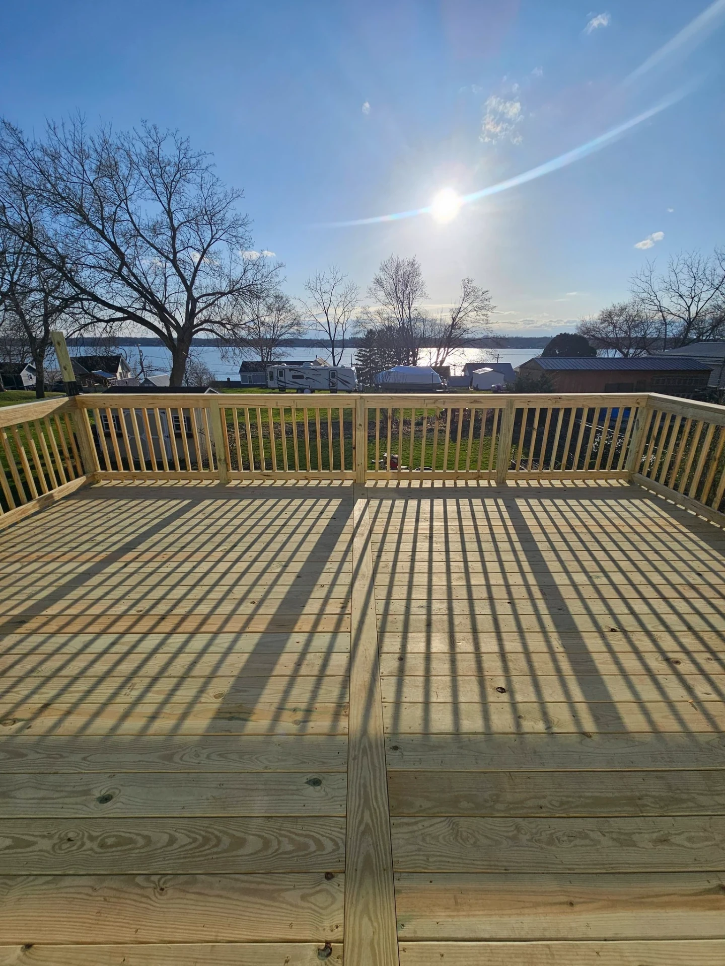 Lakefront pressure treated deck with full perimeter railings, sun flare over the water