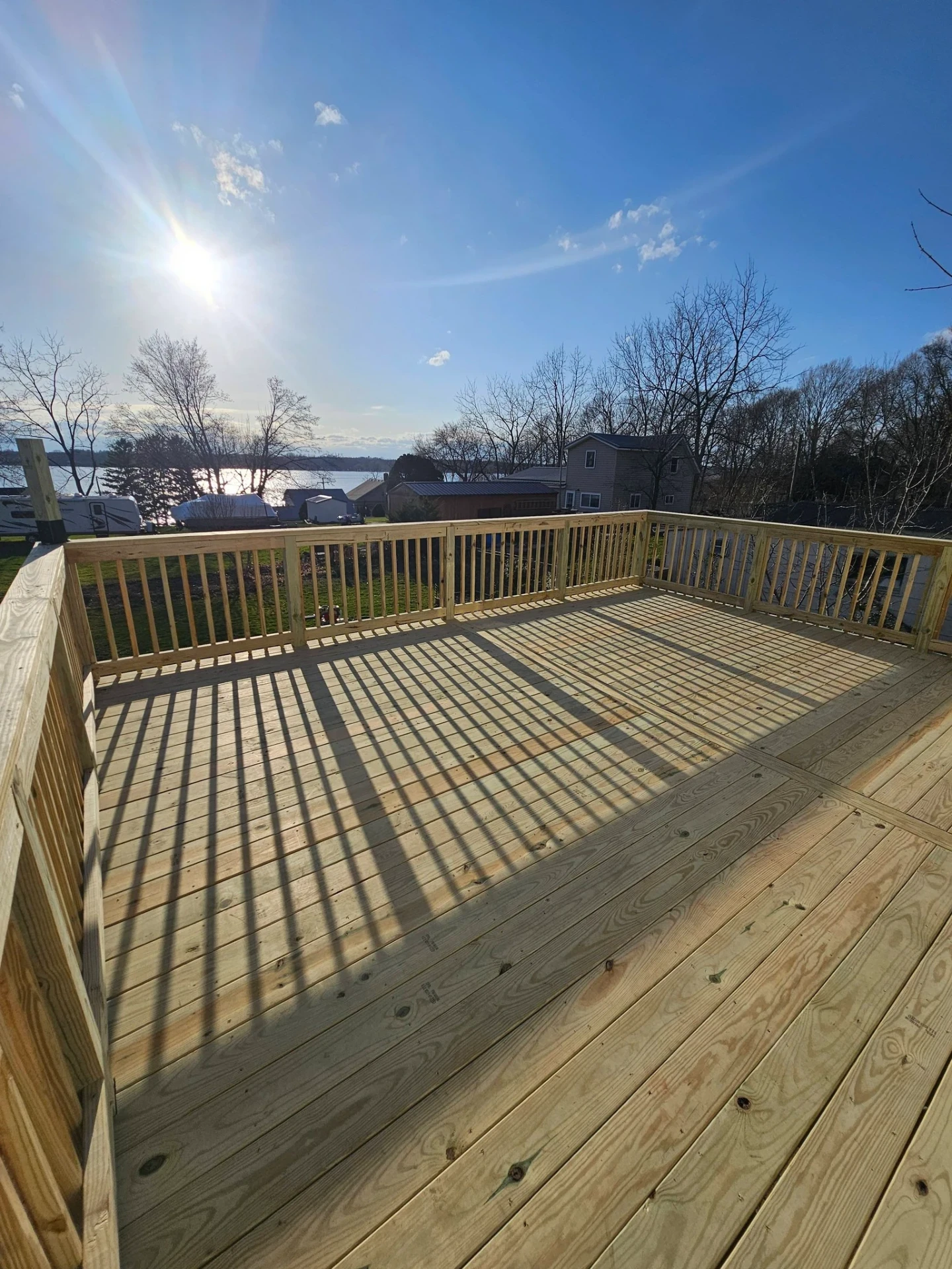 Wide lakefront pressure treated deck with railings and sunburst over the water