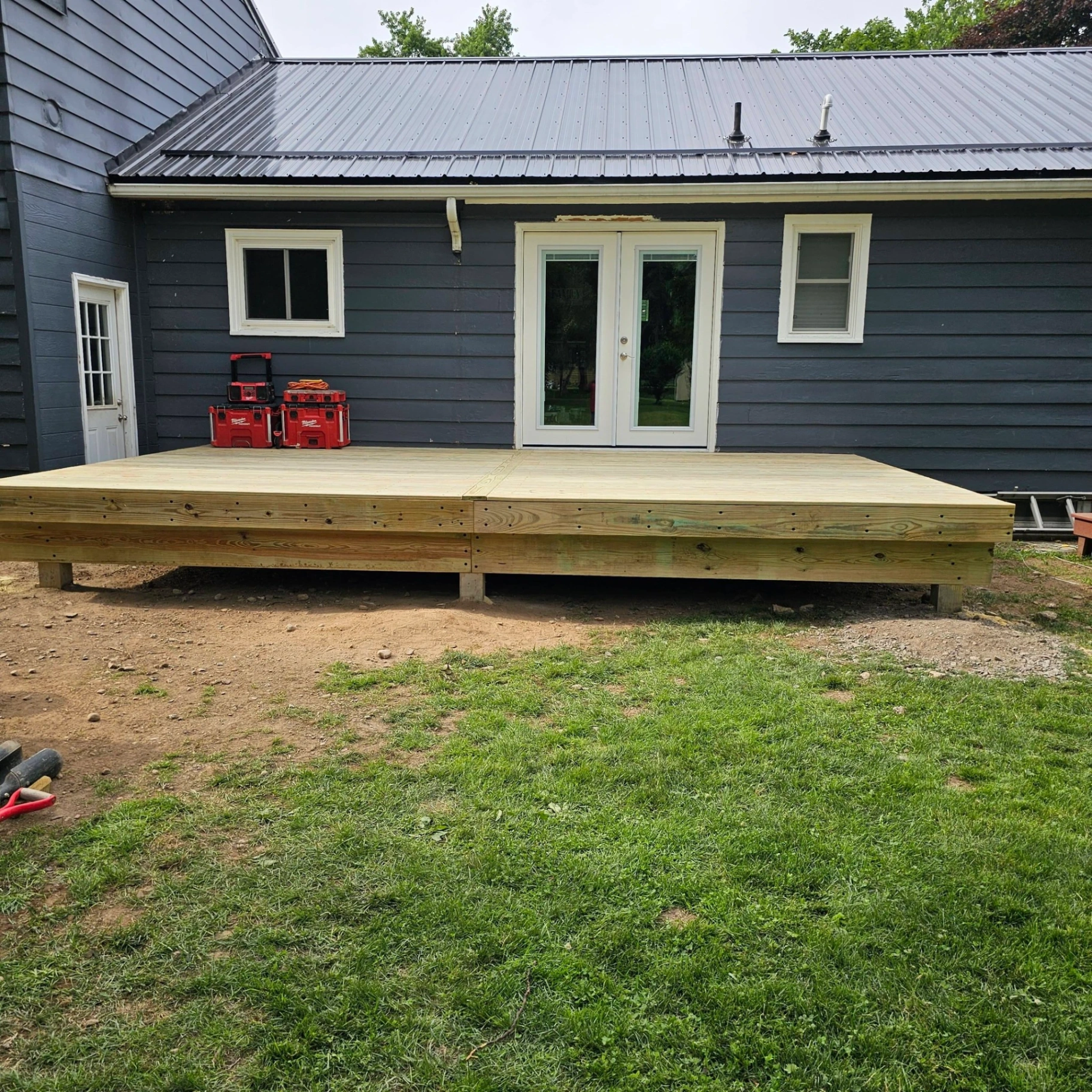 Low profile pressure treated deck off French doors on a dark blue sided home with metal roof