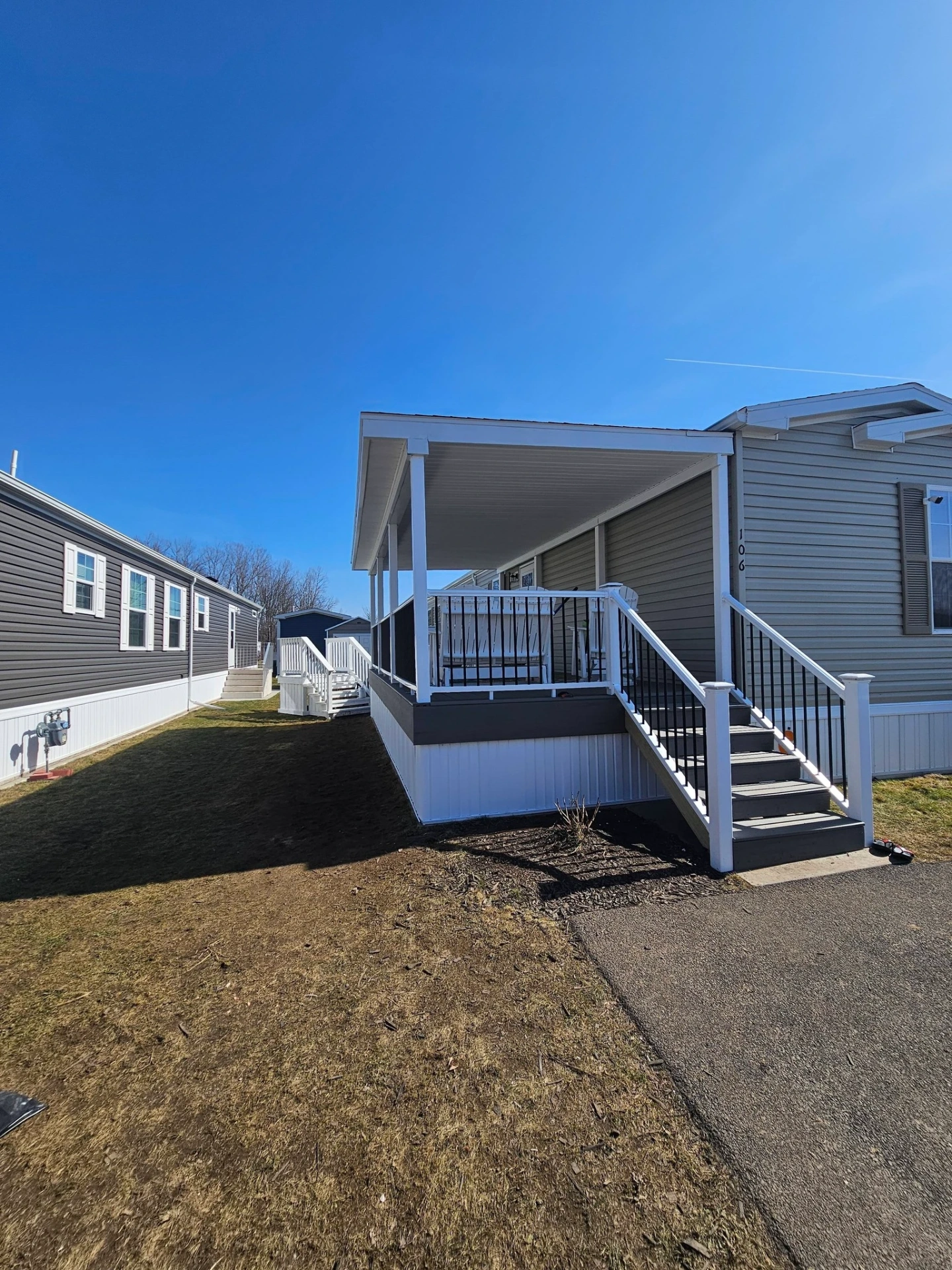 Manufactured home with new covered porch addition, white skirting and black aluminum railings on the stairs