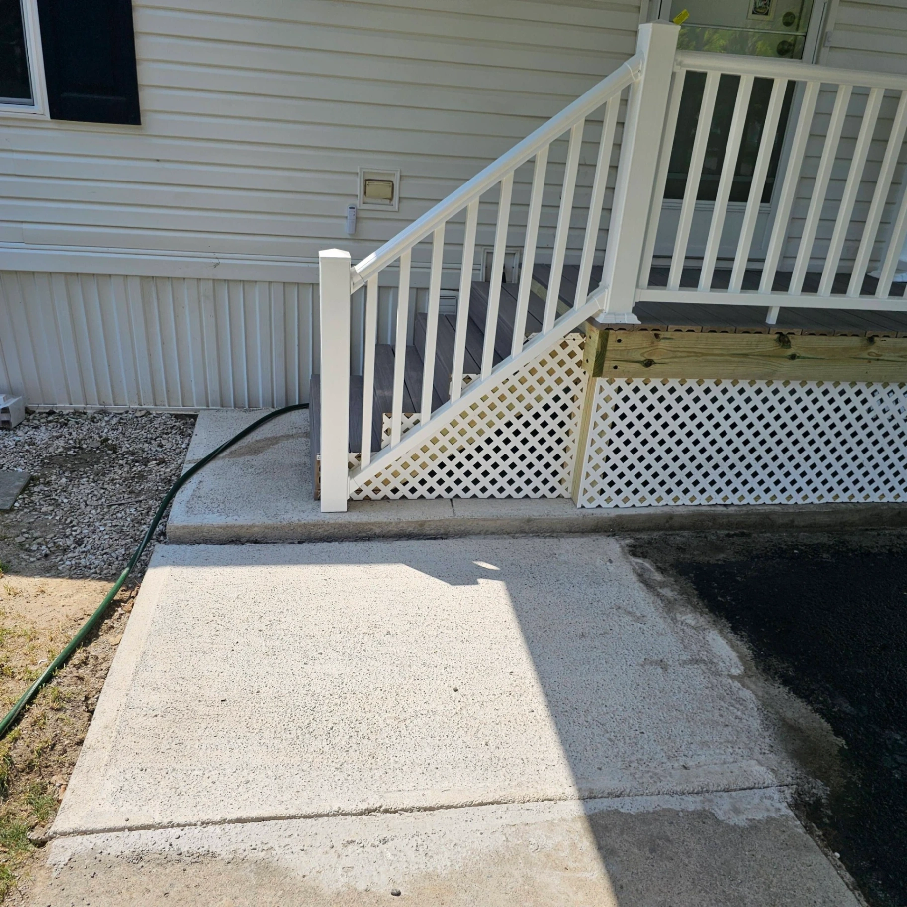 Manufactured home deck with composite decking, white aluminum railings and lattice skirting on a fresh concrete pad