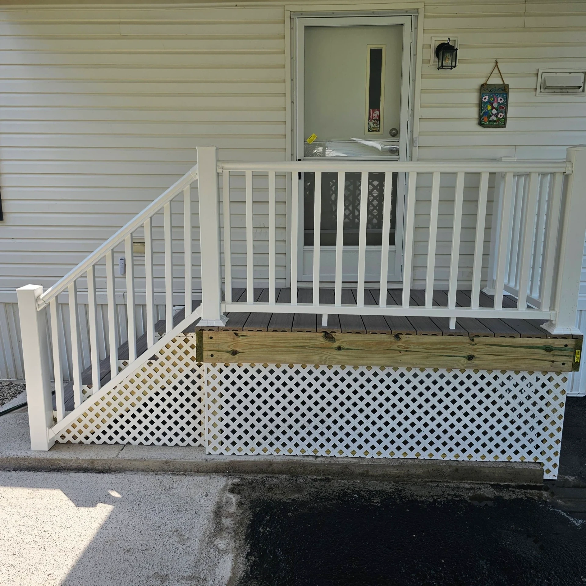 Finished manufactured home porch with white vinyl railings, gray composite decking and white lattice skirting