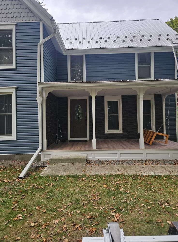 Blue sided farmhouse with a new standing seam metal roof and covered front porch