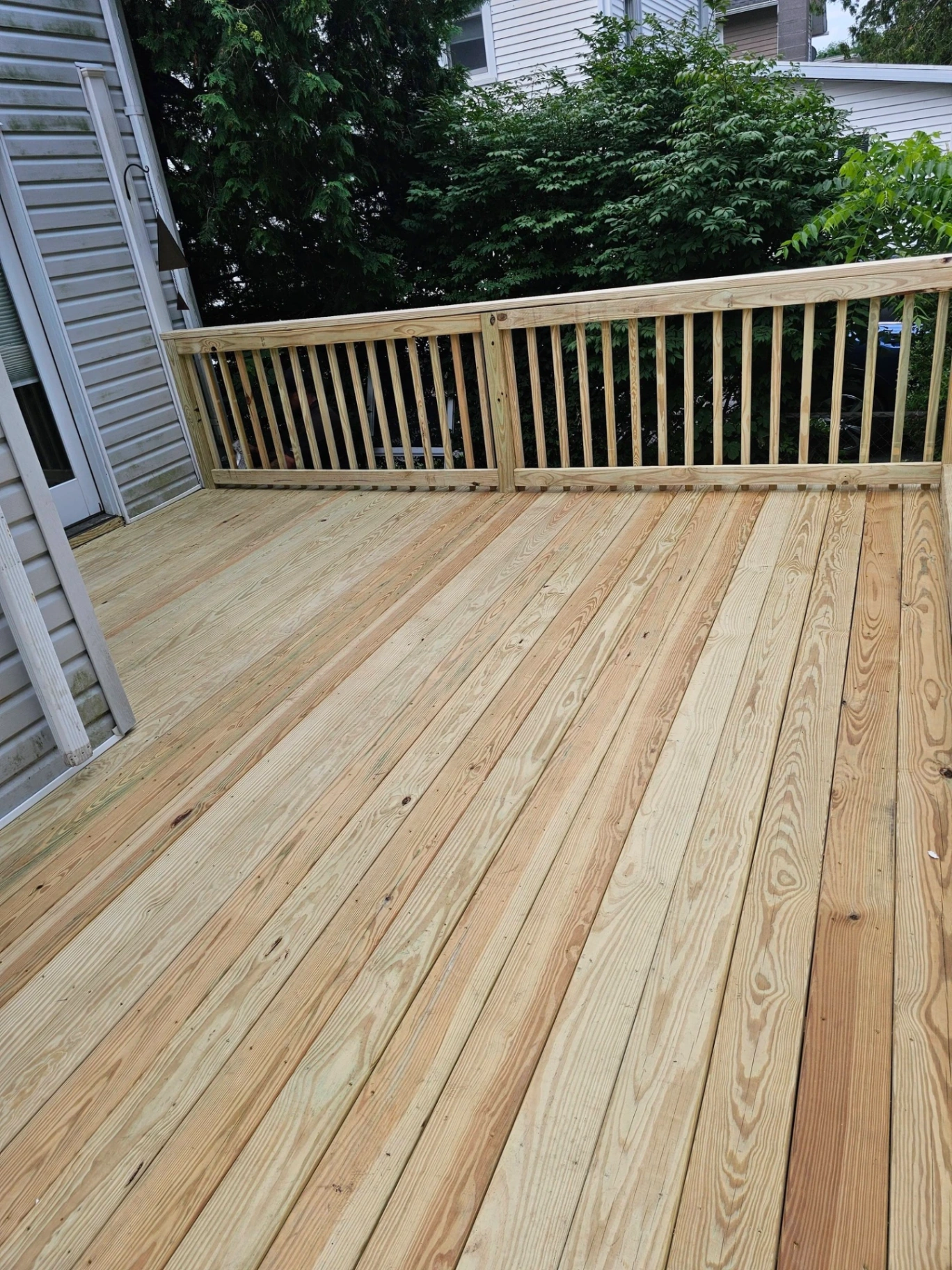 Finished side yard pressure treated deck with matching wood railings against a gray sided home