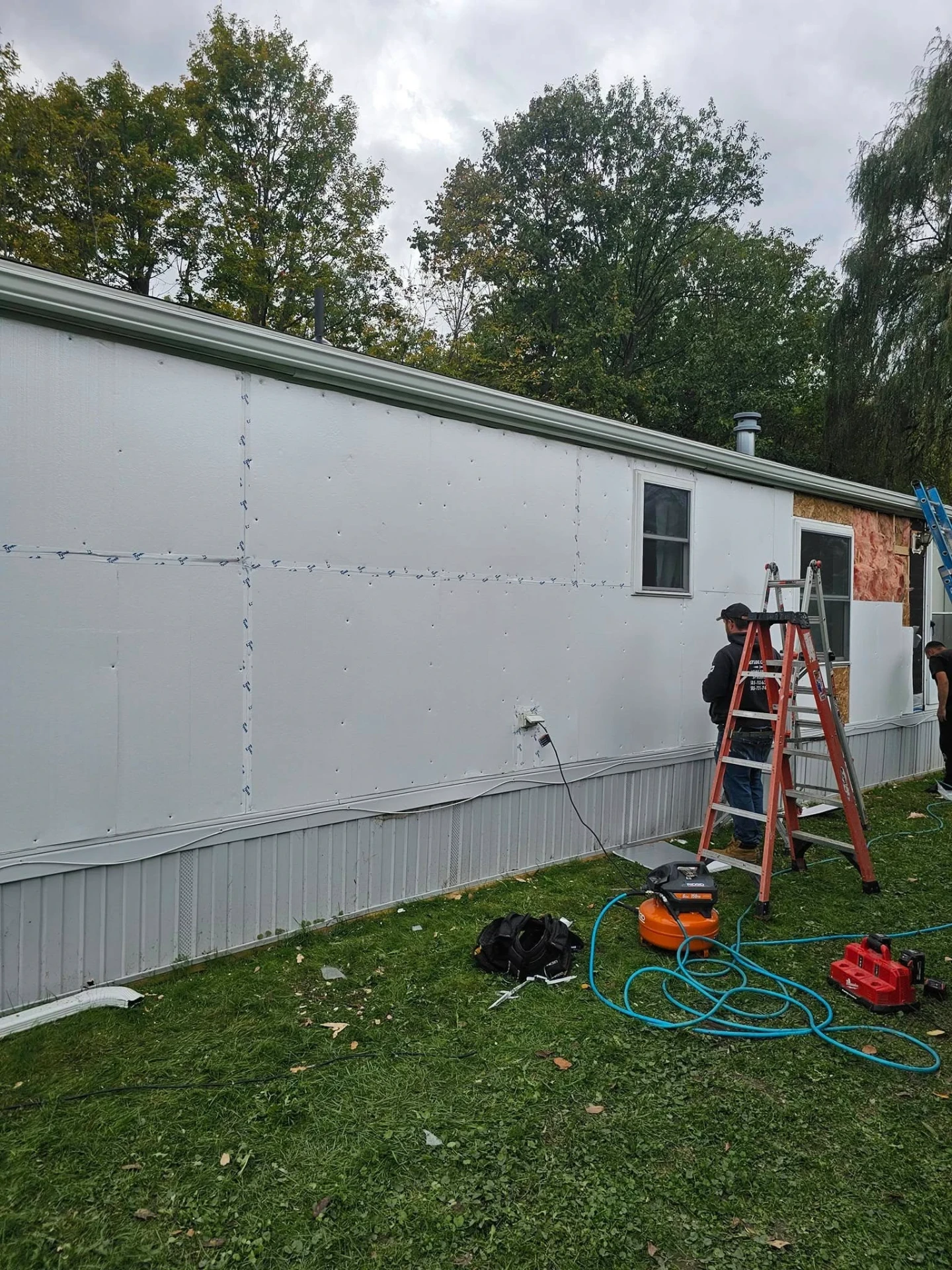 Long manufactured home wall covered in fresh house wrap with crew finishing the last section