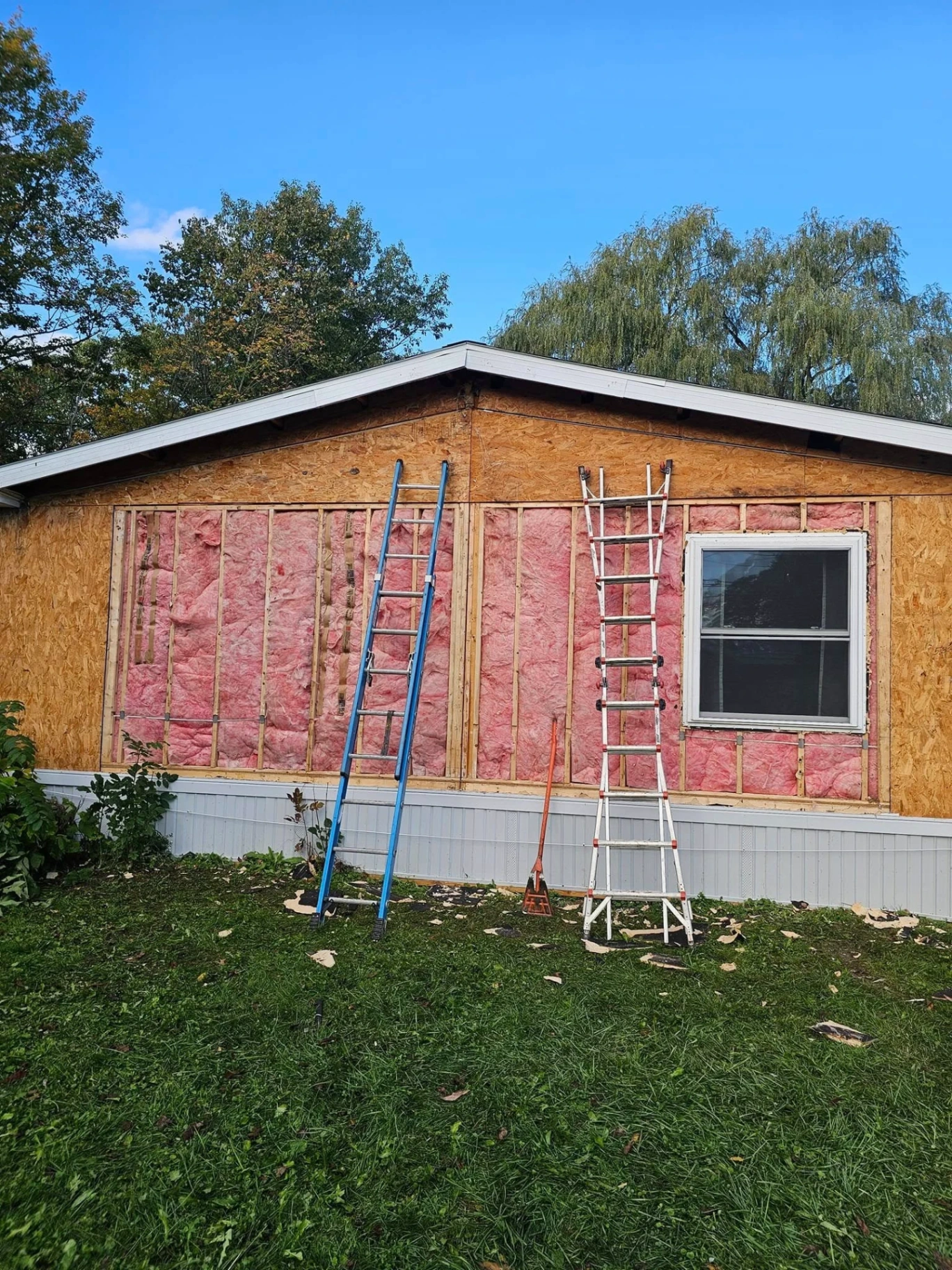 Manufactured home with siding removed showing wall studs, insulation and ladders staged for the next phase