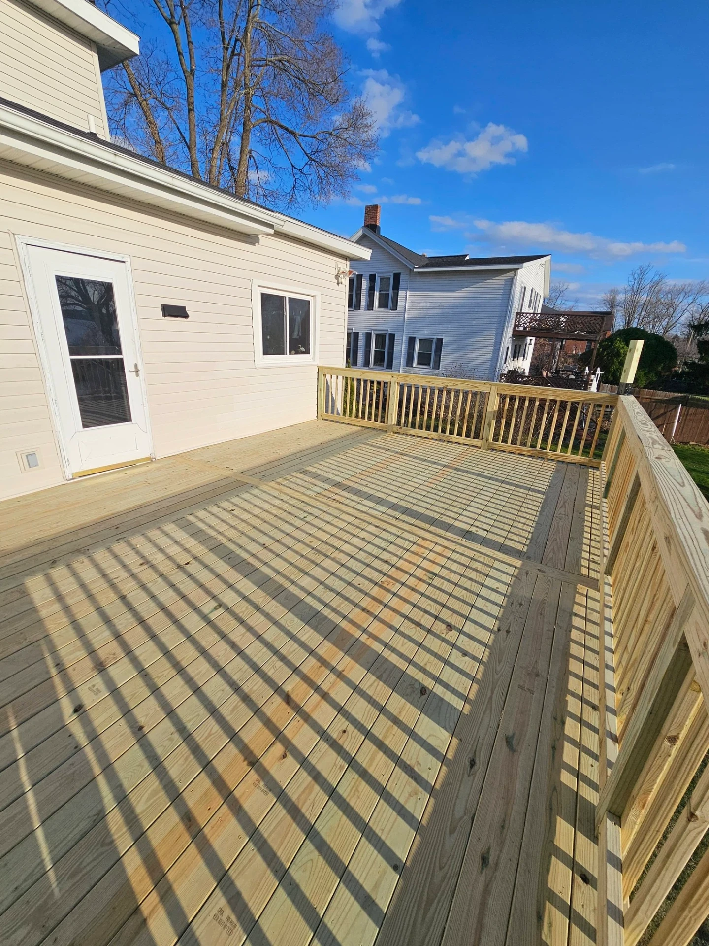 Spacious back deck with fresh pressure treated decking and full perimeter railings on a tan sided home