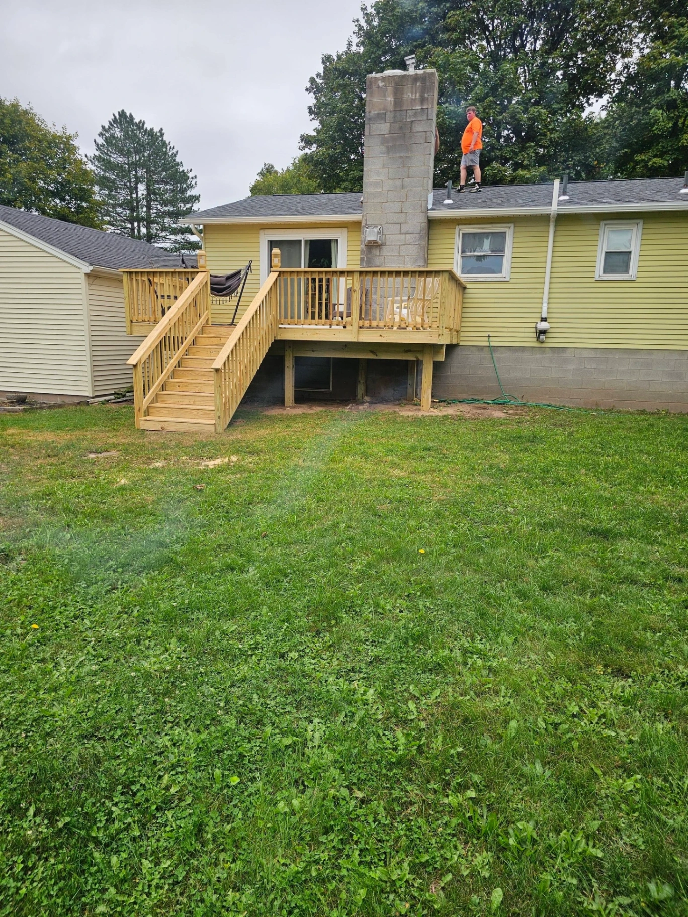 Pressure treated back deck with stairs on a yellow ranch home with stone chimney and worker on the roof